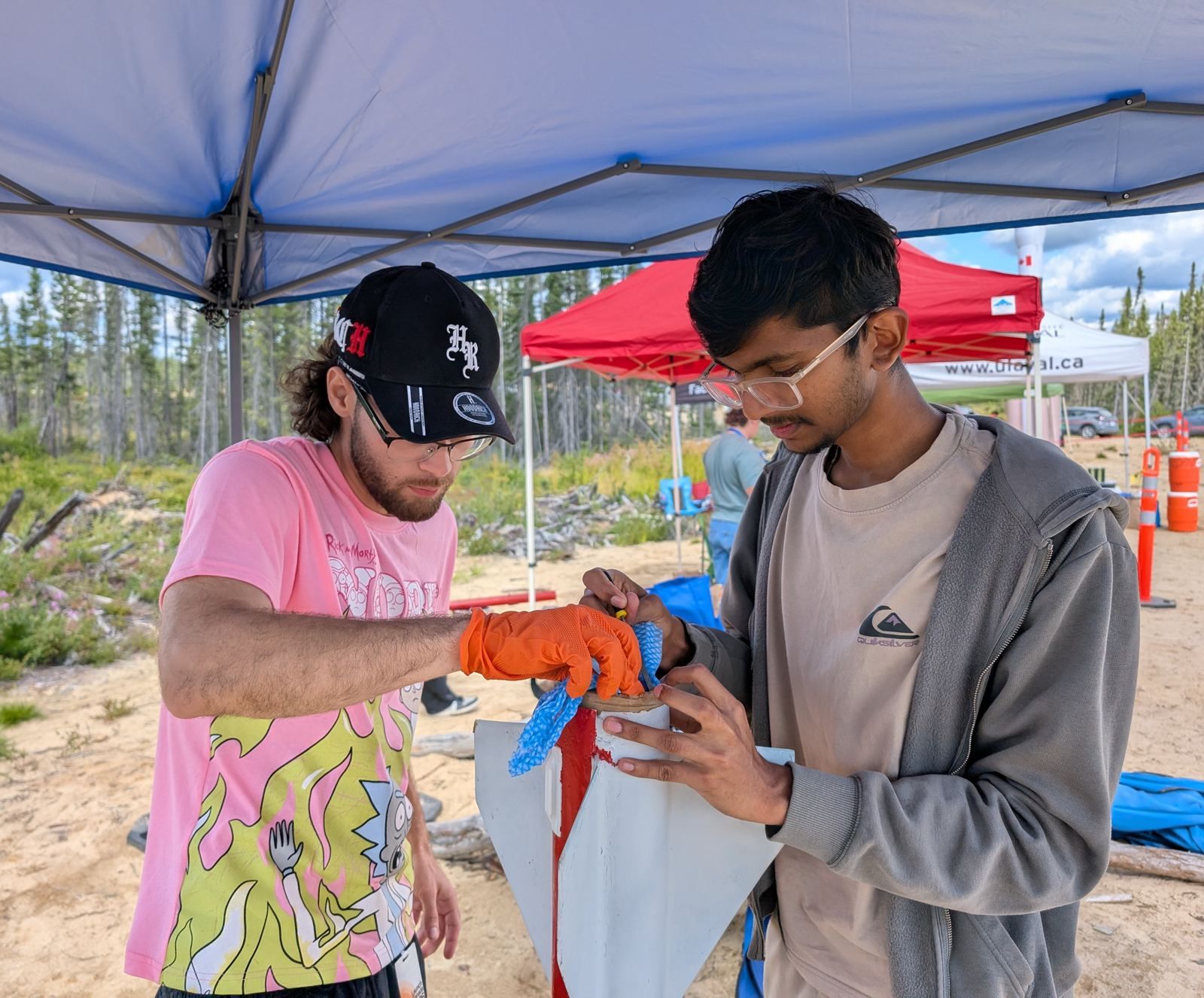 Two members in gloves working with a bottle of solvent under a tent