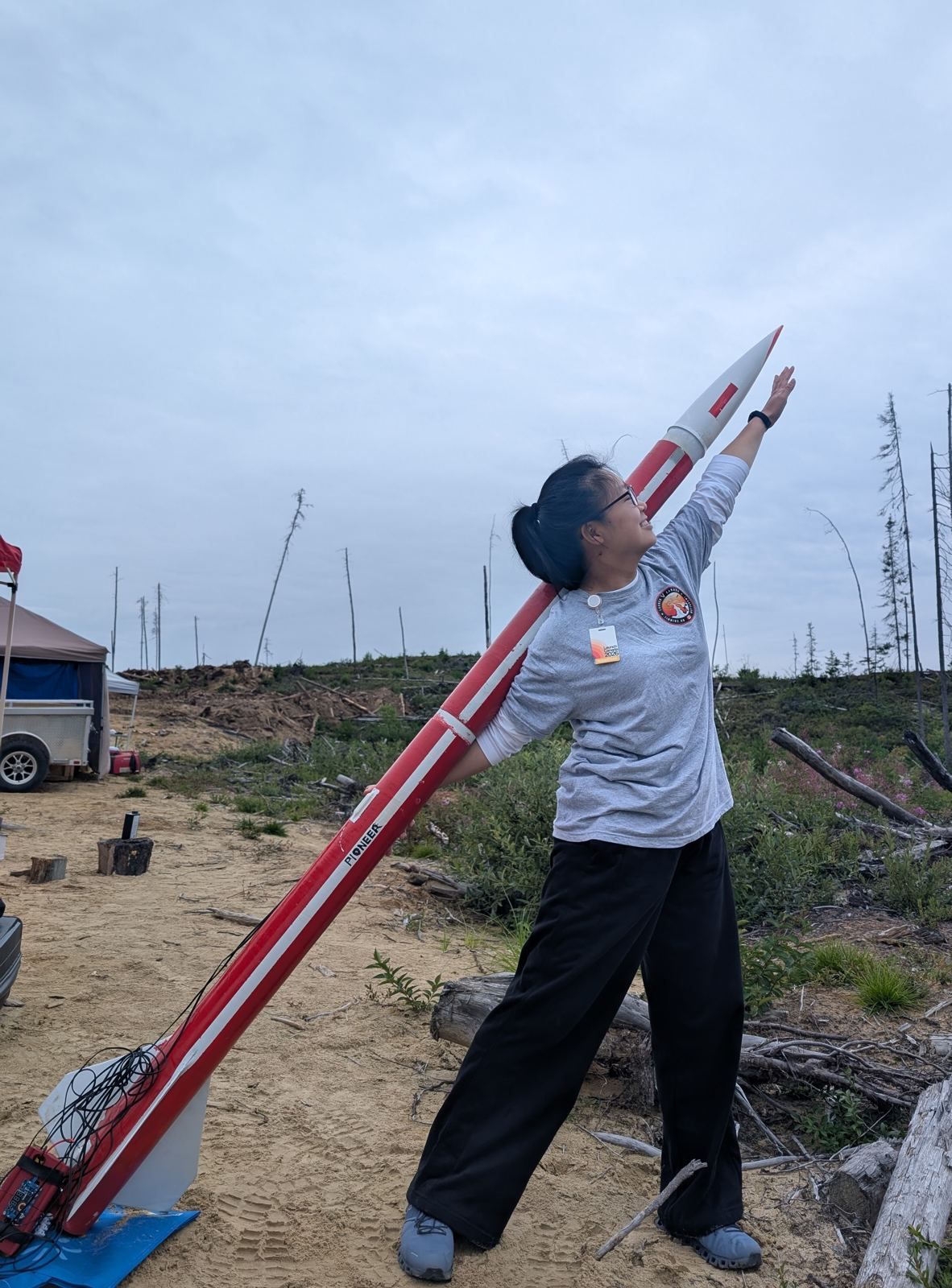 An Astra Labs member reaching up beside Pioneer, a red-and-white rocket, on the Launch Canada range