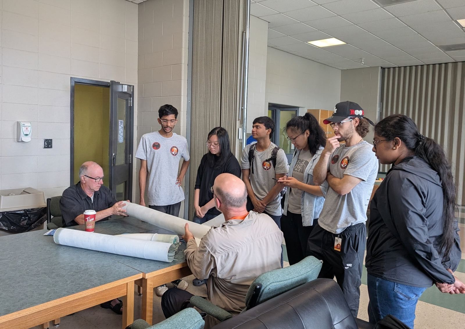 Team members in Astra Labs shirts gathered around a table while two mentors look over a rocket