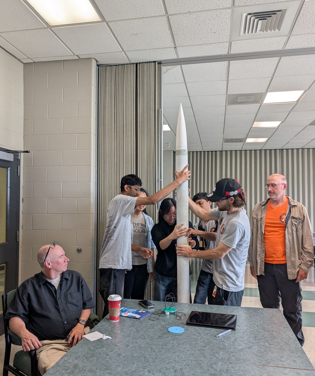 Members steadying a rocket upright while mentors look on