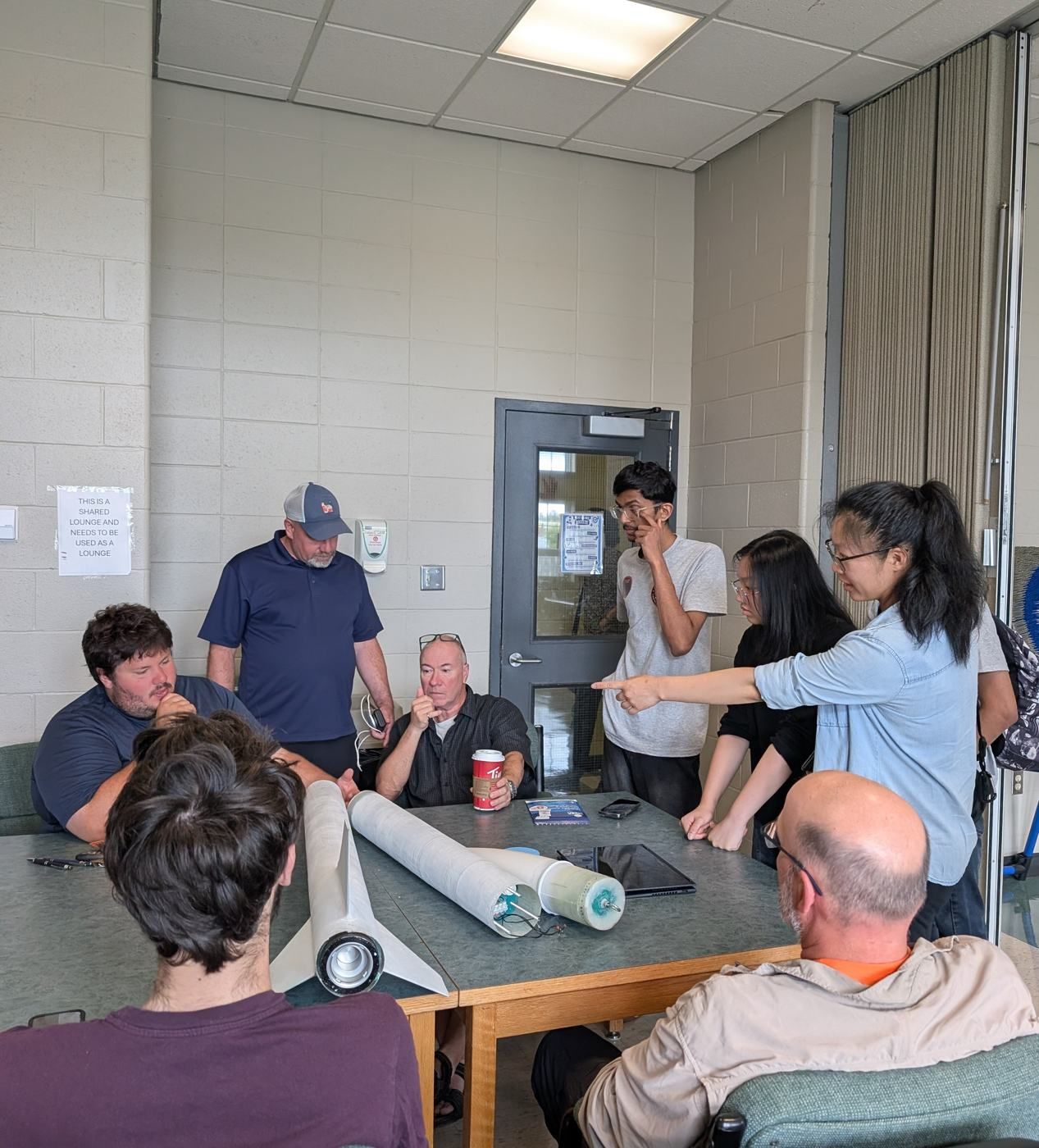 Members pointing at a rocket on a table during a mentor review