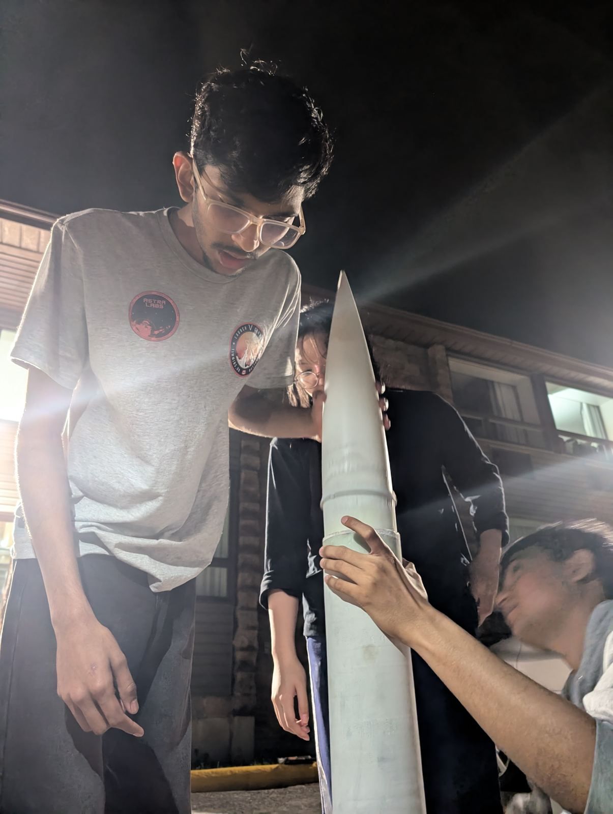 A member checking a rocket nose cone under work lights at night