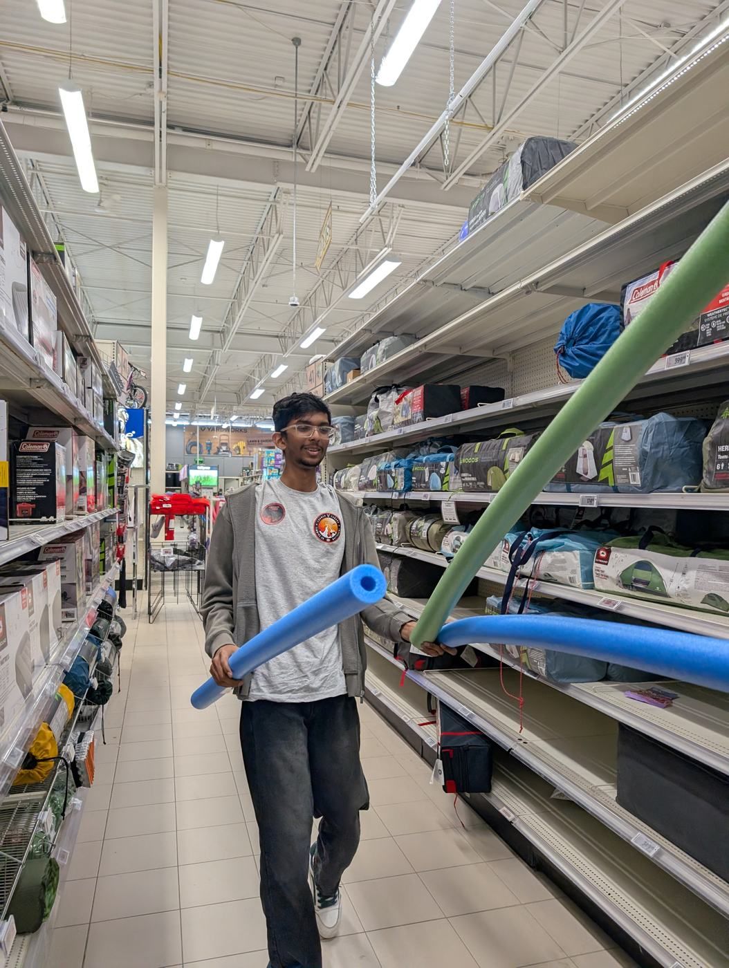 A member walking down a store aisle holding pool noodles