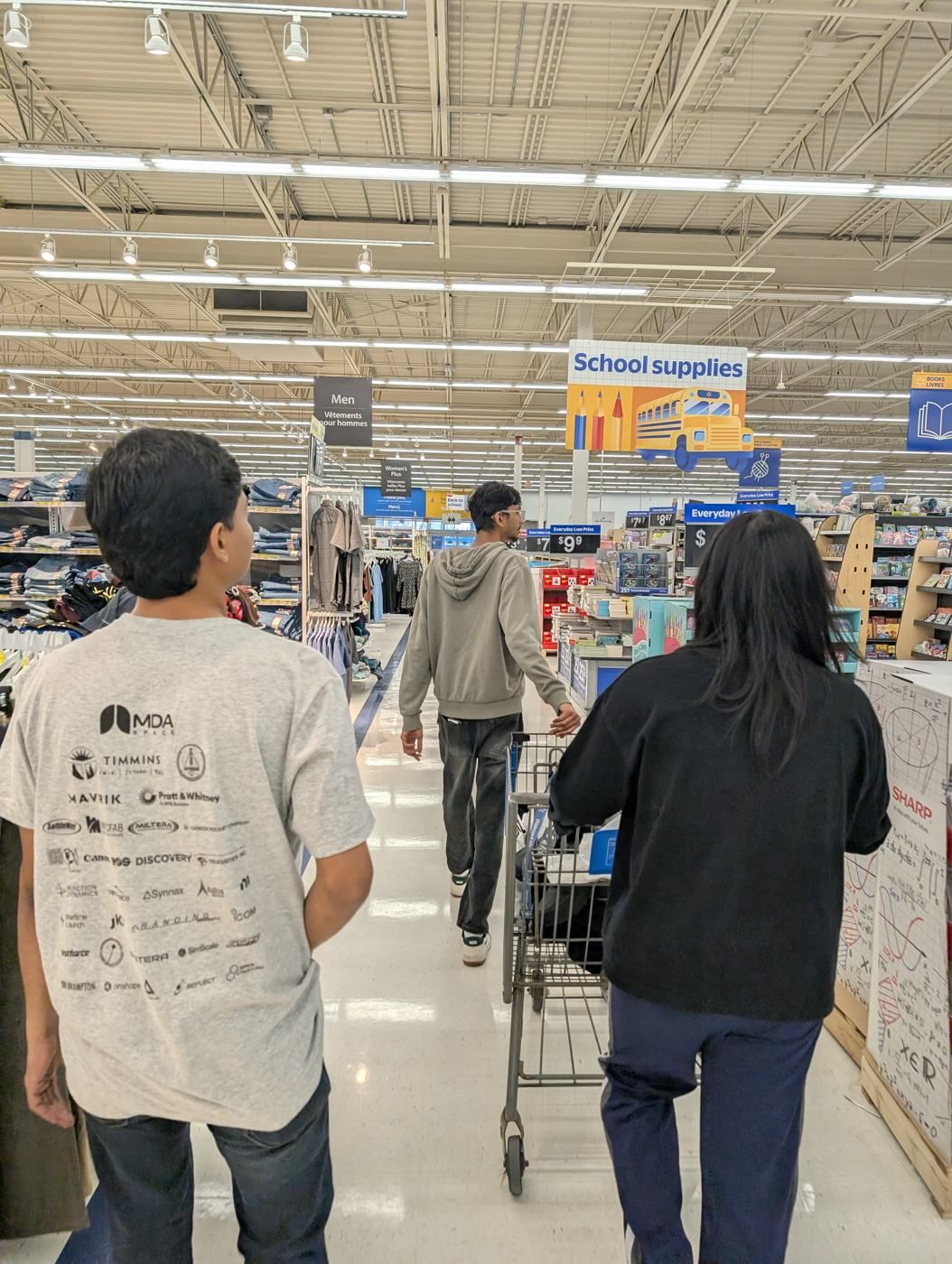 Three members walking through a store with a shopping cart